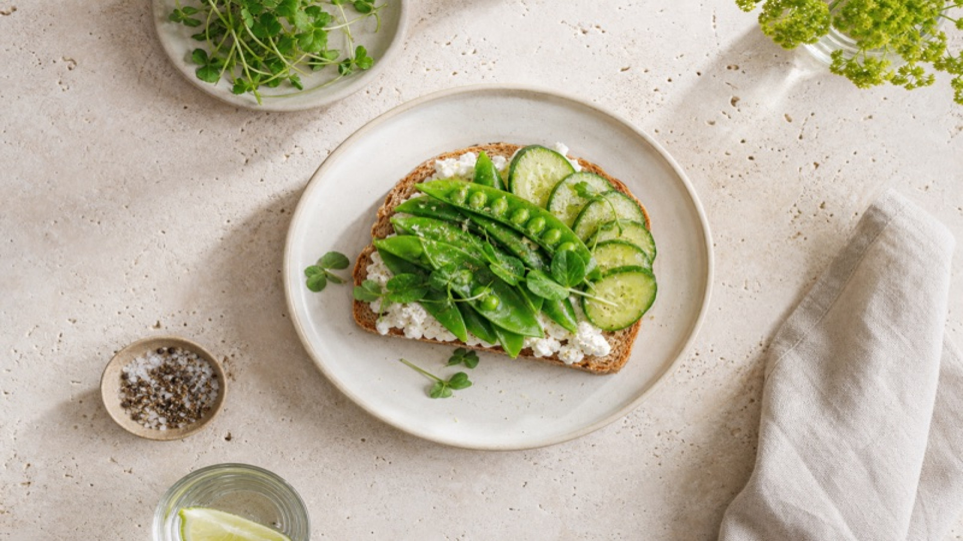 Körniger Frischkäse auf Vollkornbrot mit Zuckererbsen und Minigurken